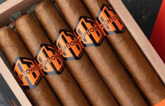 A close-up of a box of Hightower Maduro cigars neatly arranged in a wooden container. The cigars have a smooth brown wrapper and are adorned with black and orange bands featuring the Hightower logo. The premium presentation highlights the handcrafted quality of these cigars.