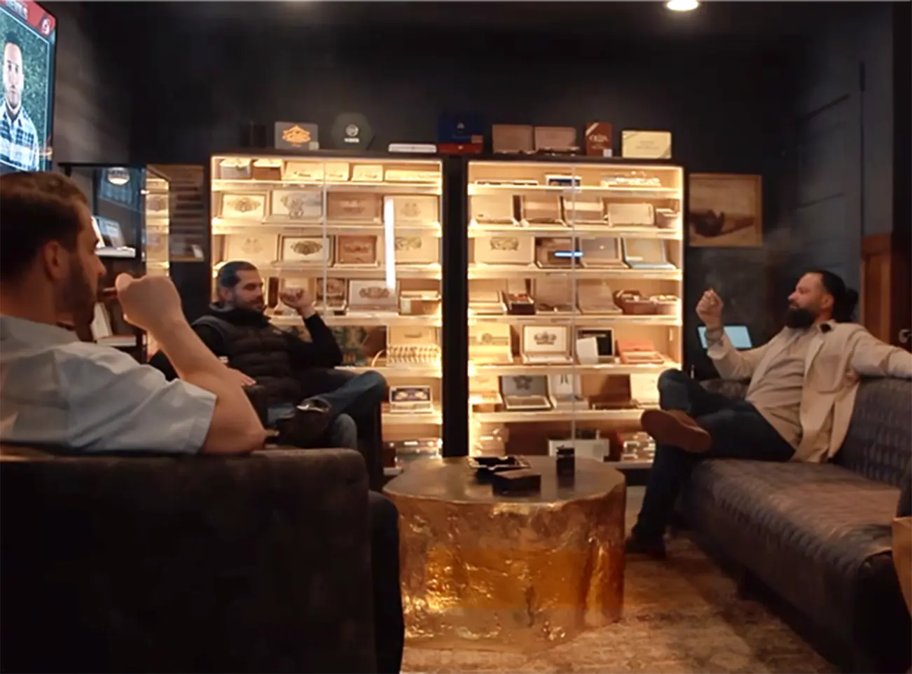 Interior of Kapnós Cigar Lounge in Sewickley, Pennsylvania, featuring three men comfortably seated, enjoying cigars in a sophisticated setting with softly lit cigar displays and a luxurious ambiance.